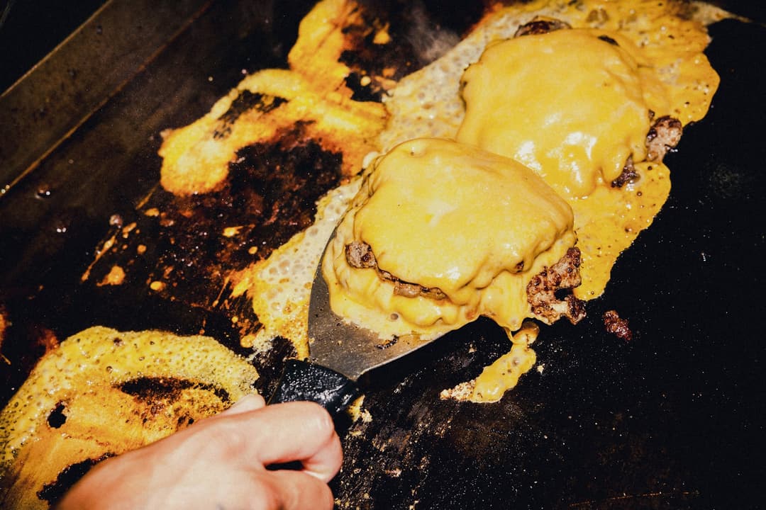Discos de carne com queijo derretido sendo virados com a espátula na chapa de ferro